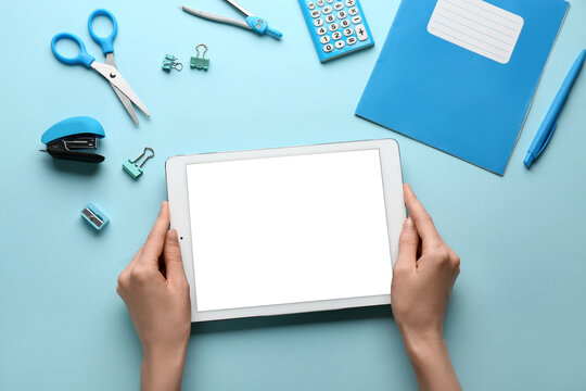 Female hands with tablet computer and school stationery on blue background