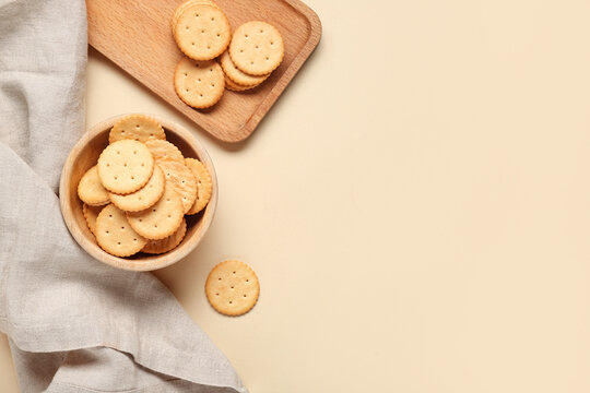 Wooden bowl and cutting board with tasty crackers on beige background