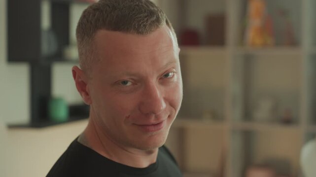 Caucasian man smiling after microcurrent therapy with visible skin glow and relaxed expression, portrait and closeup frames capture confident vibe, casual black shirt and soft studio light, shelf