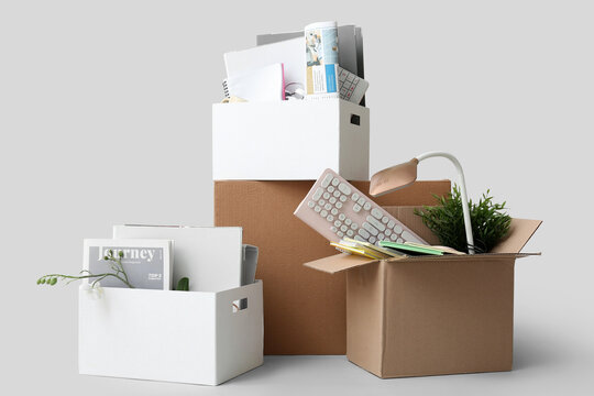 Cardboard moving boxes with office supplies, lamp and houseplants on white background