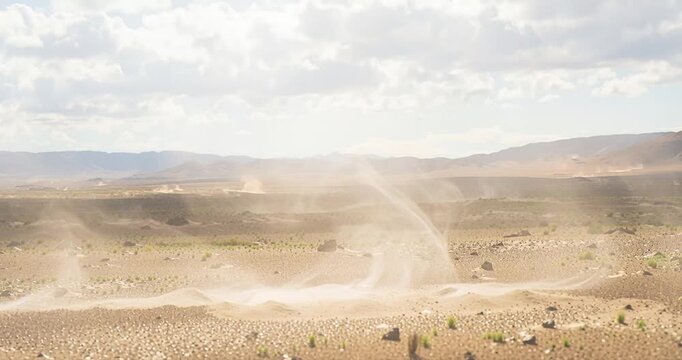 Dust devil forming above arid landscape under cloudy sky