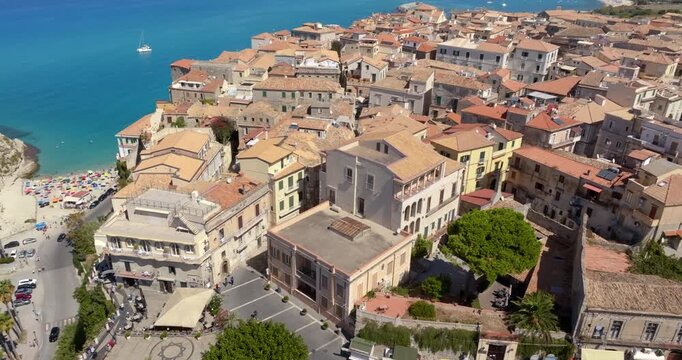 Panorama of Tropea, Calabria, Italy. The iconic Sanctuary of Santa Maria dell'Isola it's on a rocky outcrop and the historic town buildings built into the cliffside. Between them lies a turquoise bay.