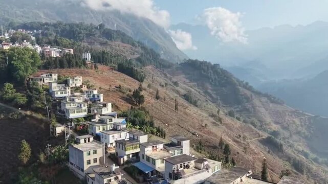 Stunning horizontal aerial shot featuring a series of traditional houses built along high mountain ridges in China. In the background, vast clouds drift over deep valleys, creating a dreamlike and maj