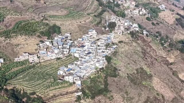 Stunning horizontal aerial shot featuring traditional rural houses nestled among vast, beautifully curved terraced fields in China. The intricate patterns of the terraces create a unique geometric bea