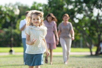Obraz premium Happiness young girl smiling and running freely expressive outdoors cheerful child in motion with family blur background in nature. Closeup portrait of joyful daughter running with parents in park.