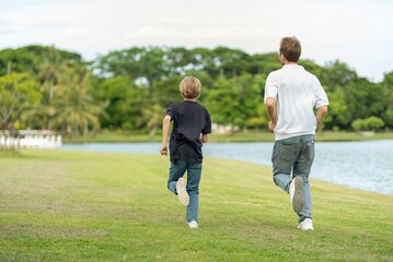 Obraz premium Smiling Father and Son Running Together in Park Enjoying Wellness Lifestyle and Healthy Outdoor Activity. Happy Parent and child Jogging Along Lakeside joyful emotional bonding family moment