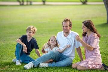 Naklejka premium Peaceful family sitting on grass in park relaxing and looking away emotional bonding moment outdoors quiet time with parents and children together. Side View Portrait of Family of Four people