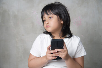 Fototapeta premium A lonely and unhappy young Asian girl holding a smartphone while staring blankly to the side.