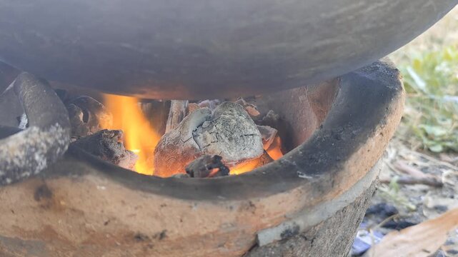 Burning firewood in a charcoal stove for cooking, with glowing orange flames and blazing hot coals.