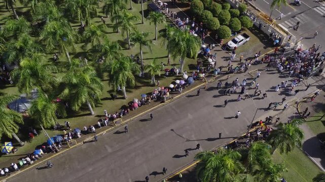Wide drone establishing shot of massive crowd of pilgrims forming long line on grounds of Hig&uuml;ey Basilica, Dominican Republic. Aerial top-down view