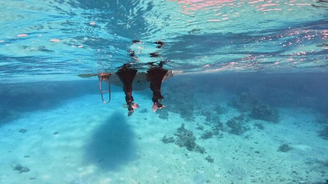 Motorboat propellers below the clear sea water surface above white sand seabed. Slow motion underwater view