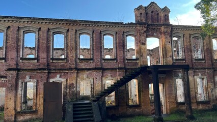 Facade of an abandoned brick building with an external staircase on a sunny day.