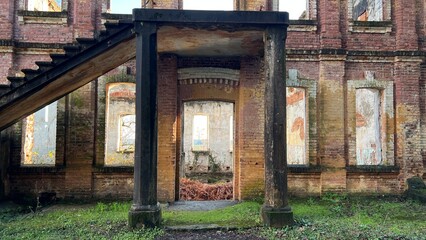 Facade of an abandoned brick building with an external staircase on a sunny day.