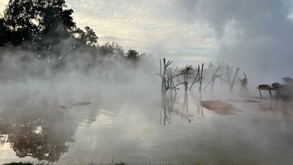 A horizontal photograph of a natural landscape, depicting the surface of a hot thermal spring or mineral pool, shrouded in dense steam. The Kyndygsky Springs geothermal area in Abkhazia.