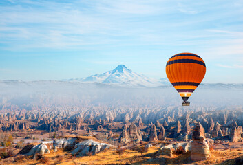 Hot air balloon flying over Cappadocia Snowy Erciyes Mountains in the background - Cappadocia, Turkey