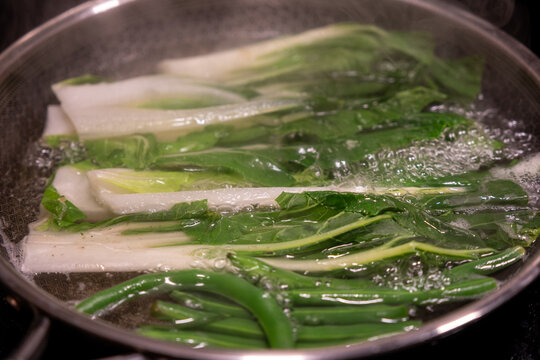 Bokchoy vegetable is being boiled in water in a pan