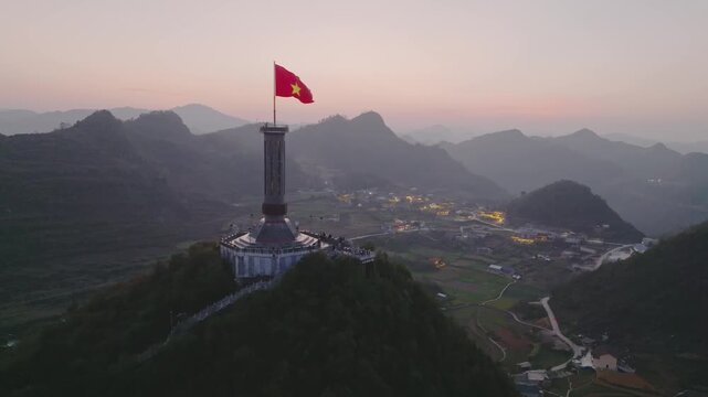 Aerial twilight view of Lung Cu Flag Tower rising above green valleys, villages, and layered limestone mountains.