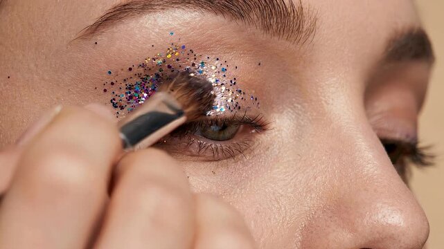 Woman applying glitter eyeshadow in close-up sequence. Caucasian female using brush to enhance eyelid with sparkling powder. Beauty makeup tutorial demonstrating festive cosmetic routine for