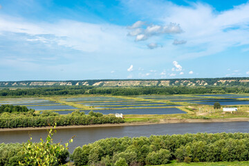 Obraz premium A river flows through a grassy green plain, and hills are visible in the background. The sky is overcast, giving the scene a serene atmosphere.