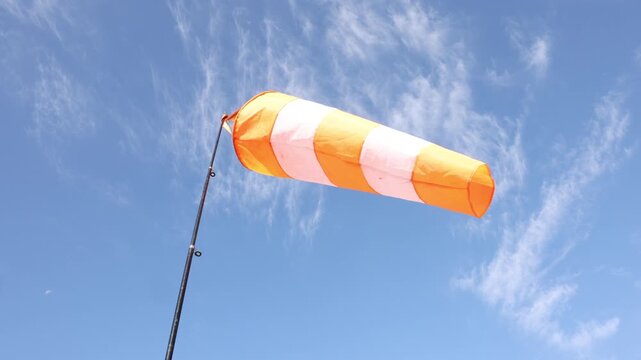 orange and white striped windsock indicating wind direction on pole against a clear blue sky with light clouds, concept of weather monitoring, aviation, airfield safety