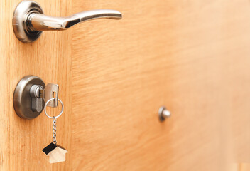 Silver house key in wooden door, with little house keyring, opening the door to a new house, home, investment, real estate concept, space for text.