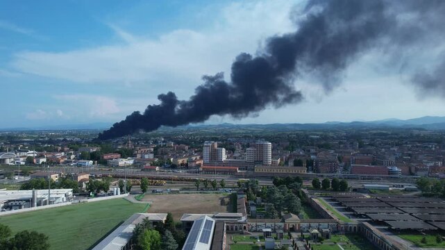 Fidenza, Po Valley showing dense black smoke from a plastic factory fire spreading toxic dioxin pollution across urban districts and surrounding agricultural land threatening food safety and po