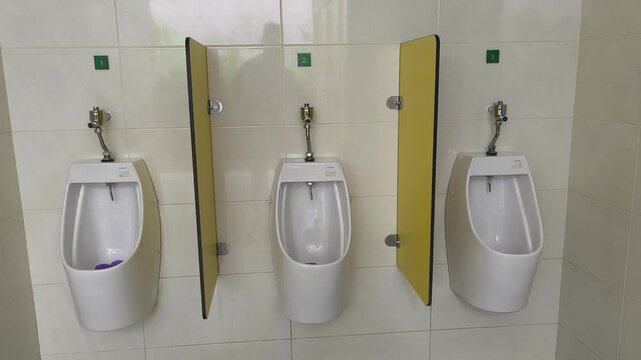 A row of clean ceramic urinals installed in a public men's restroom. Slim privacy walls are placed between each unit to ensure comfort and discretion. The design is modern and functional.