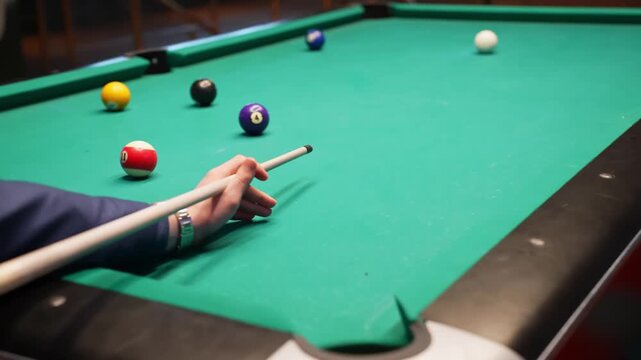 Pool player misses a precise shot, cue stick over green felt as scattered balls remain on the table in a bar billiards game with shallow depth-of-field.