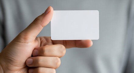 Hand holding a blank white card in front of a person wearing a gray shirt