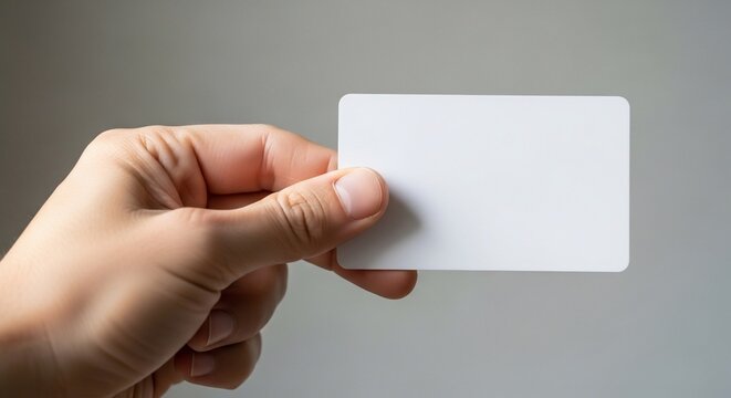 Hand holding a blank white card against a plain gray background from a front viewpoint