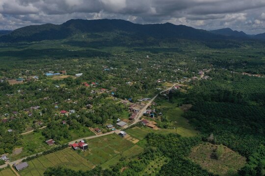 Panoramic aerial perspective of Karang Agung village in North Kalimantan, Indonesia, showcasing the provincial road infrastructure cutting through residential settlements and lush rice paddies against