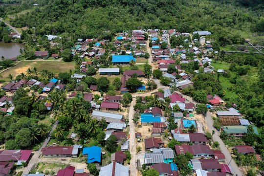Panoramic aerial view of Kelincauan village in Sekatak, North Kalimantan, featuring a community soccer field and residential housing along the winding Buji River. This drone perspective highlights the