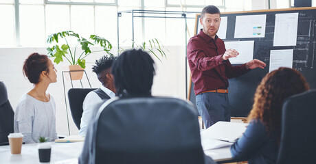 Man, presentation and talking with team in office for creative startup, planning and venture pitch. Speaker, staff or briefing with chalkboard, business ideas and brainstorming for marketing strategy © peopleimages.com