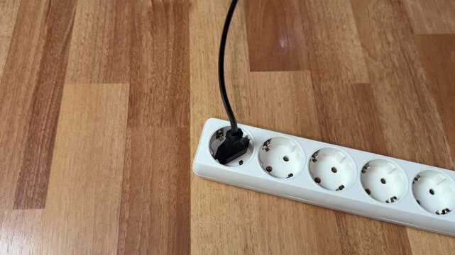 Person hand plugs electrical appliance into surge protector and suddenly jerks away due to electric shock. Using unsafe electrical appliance. Risk of injury and death from electric shock