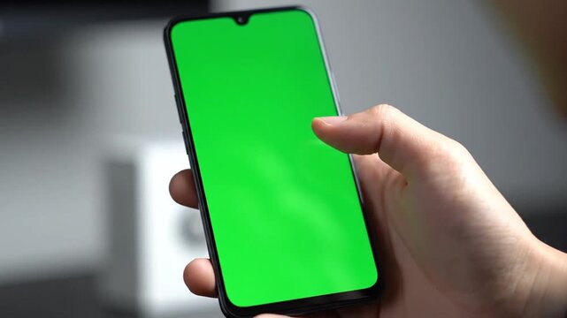 A person's hand holding a modern smartphone with a vibrant green screen, ready for digital content insertion or chroma key effects.