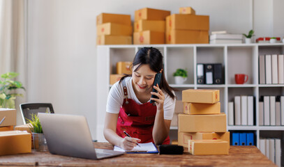 Asian woman small businesses SME owners asian female entrepreneurs call phone on receipt box and check online orders to prepare to pack the boxes, sell to customers, SME business ideas online. 