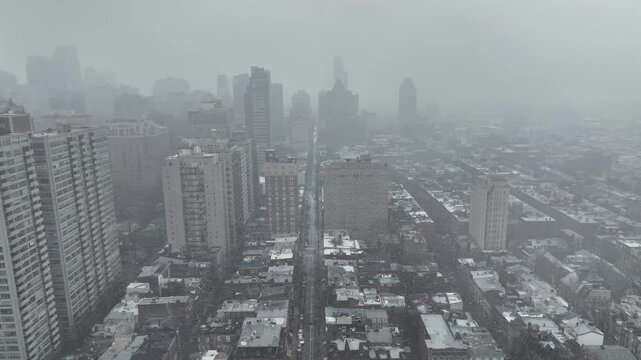 Philadelphia skyline covered in fog, showing dense urban streets, high-rise buildings, cold weather atmosphere and muted city tones. Winter scene from above. Aerial backwards wide shot.