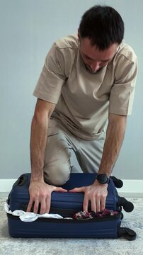 A tense traveler tries to close an overfilled suitcase