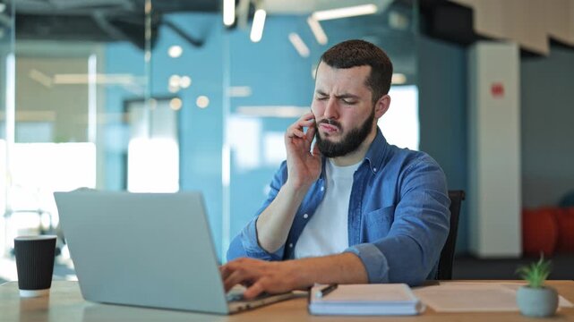 Young man working on laptop experiences sudden, sharp toothache in office. Discomfort and pain interrupt focused work. Urgent health problem causing worry and unhappiness.