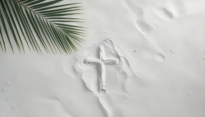 A cross drawn in the sand on a peaceful beach with a palm leaf