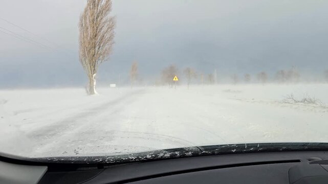 Driving a passenger car in a snowstorm. Traveling through the countryside in winter conditions. Sunny weather contrasts with snow blown from the fields, obscuring visibility. 