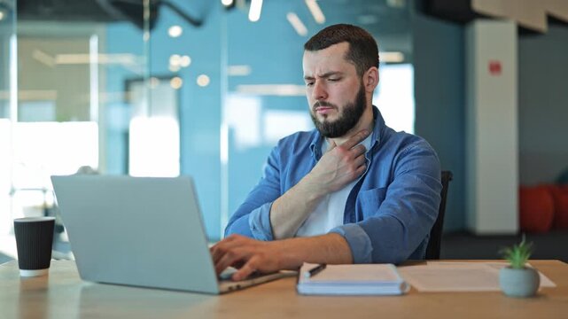 Unwell professional experiences sore throat while diligently working on laptop in modern office environment. Feeling discomfort and pain, focused on job despite feeling sick.