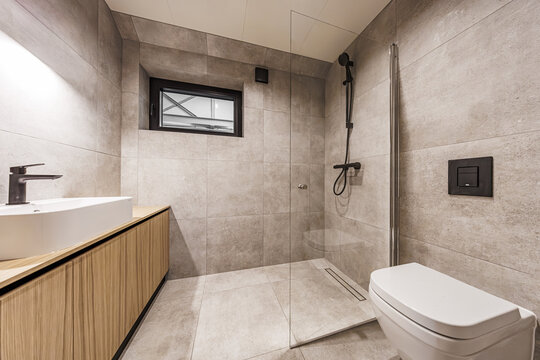 Stylish bathroom interior with light stone tiles, wood vanity, vessel sink, walk-in shower, and matte black fixtures. Ample copy space on walls