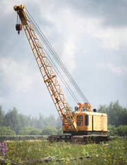 Industrial crawler crane positioned near water in a rural landscape, showcasing heavy construction machinery, long boom reach, and large-scale engineering operations.