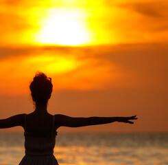 Fototapeta premium A woman is standing on the beach and looking at the sun