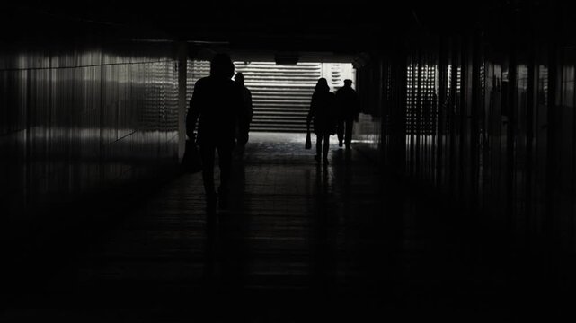 Silhouettes crowd peoples walking up stairs from subway. Backlit pedestrians go up and down steps underpass in winter. Underground passage. City life. Light at end tunnel, dark figures people wailk.