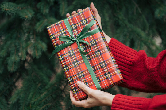 Hand holding wrapped Christmas gift outdoors with plaid ribbon