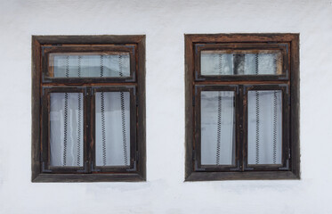 Obraz premium Two vintage wooden windows with white curtains on a rustic white wall