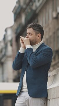 A man in a blue jacket plays the harmonica on the street looking up
