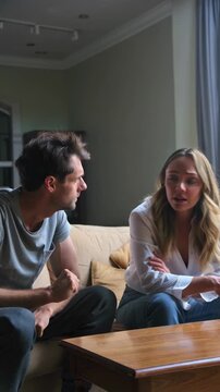 Frustrated couple engaged in a serious conversation on a sofa, reflecting relationship conflict at home, vertical shot